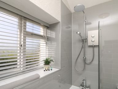 A bathroom shower area with a rain showerhead handheld shower and window with blinds at Carvannel Cottages North Cliffs near Portreath