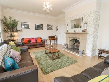 A living room with brown leather sofas a wooden coffee table with glasses and a bottle on a green rug by a stone fireplace at Heatherbrae in Middleton-In-Teesdale