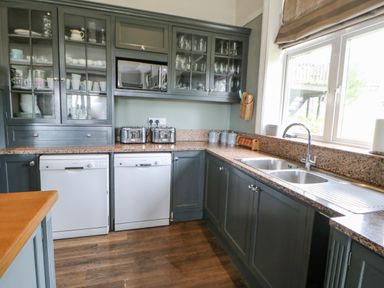 A kitchen with dark cabinets a double sink two dishwashers toasters and glass front cabinets at Heatherbrae in Middleton-In-Teesdale