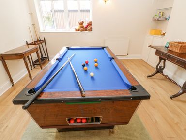 A blue pool table with cues and balls in a room with wooden tables and a window with teddy bears at Heatherbrae in Middleton-In-Teesdale