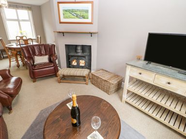 A living room with leather chairs a round wooden table with a bottle and glasses a fireplace and a television on a wooden stand at Heatherbrae in Middleton-In-Teesdale