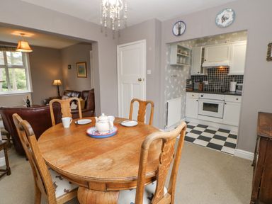 A dining area with a wooden table and chairs next to a kitchen with black and white tiled floor at Heatherbrae in Middleton-In-Teesdale