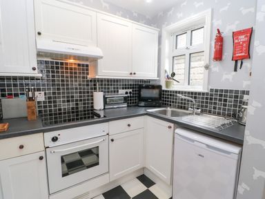 A kitchen with white cabinets black tiled backsplash a stove oven sink and small appliances at Heatherbrae in Middleton-In-Teesdale