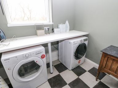 A laundry room with a washing machine and dryer under a white countertop and a wooden cabinet on a black and white checkered floor at Heatherbrae in Middleton-In-Teesdale
