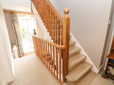 A staircase with wooden banister and beige carpet leading up from a hallway with door to outside at Heatherbrae in Middleton-In-Teesdale