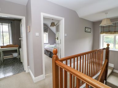 A hallway with wooden stair railing and open doors leading to a bedroom and tiled room at Heatherbrae in Middleton-In-Teesdale