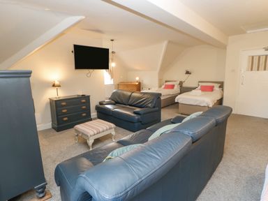 A living area with two leather sofas two single beds a footstool a chest of drawers and a wall-mounted TV at Heatherbrae in Middleton-In-Teesdale