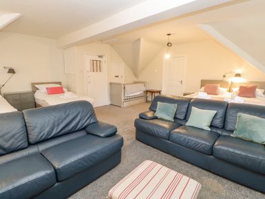 A room with two blue leather sofas a striped ottoman two single beds a double bed a crib and bedside tables at Heatherbrae in Middleton-In-Teesdale