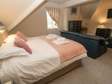 A bedroom with a bed with pink pillows and blanket a black sofa and dressers at Heatherbrae in Middleton-In-Teesdale