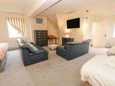 A living room with two black leather sofas a chest of drawers a wall-mounted television and beds at Heatherbrae in Middleton-In-Teesdale