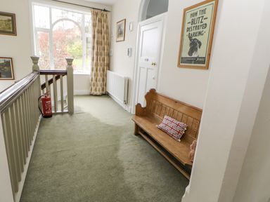A hallway with a wooden bench and cushion near a door and window with floral curtains at Heatherbrae in Middleton-In-Teesdale