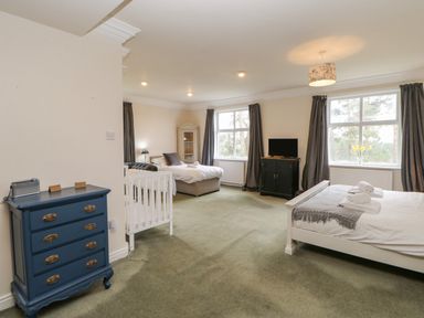A bedroom with two beds a crib a blue chest of drawers a cabinet a television and windows with curtains at Heatherbrae in Middleton-In-Teesdale