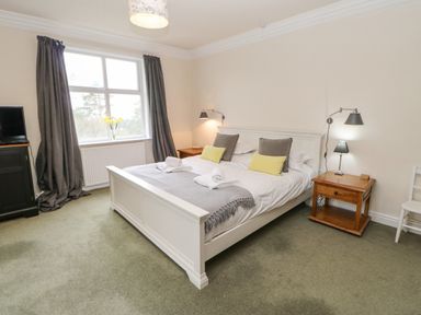 A bedroom with a white bed, wooden side tables, lamps, gray curtains, and a window with flowers at Heatherbrae in Middleton-In-Teesdale