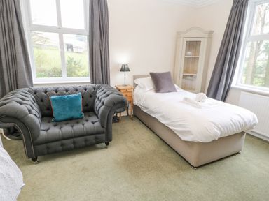 A bedroom with a single bed a grey sofa a wooden bedside table lamp and large windows at Heatherbrae in Middleton-In-Teesdale