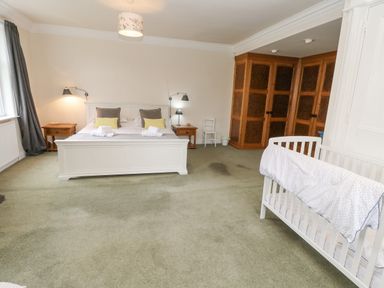 A bedroom with a double bed two bedside tables a baby crib wooden wardrobes and green carpet at Heatherbrae in Middleton-In-Teesdale
