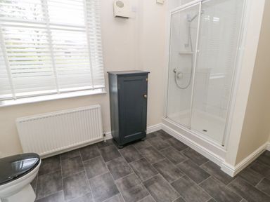 A bathroom with a shower enclosure a black storage cabinet and a window with blinds at Heatherbrae in Middleton-In-Teesdale