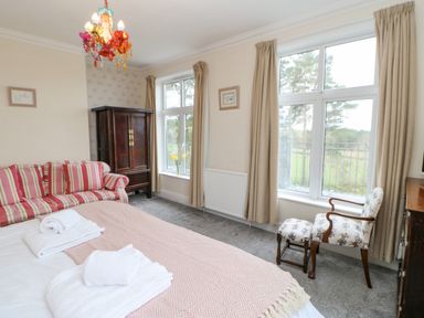 A bedroom with a bed with towels a striped armchair a wooden cabinet two windows with beige curtains and a floral armchair at Heatherbrae in Middleton-In-Teesdale