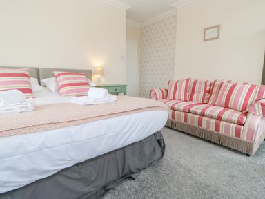 A bedroom with a bed and striped sofa with a green bedside table at Heatherbrae in Middleton-In-Teesdale