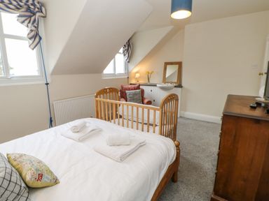 A bedroom with a double bed and a wooden crib near two windows an armchair and a wooden dresser with a tv at Heatherbrae in Middleton-In-Teesdale