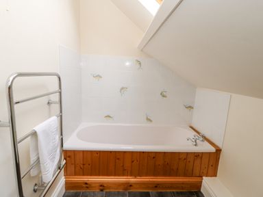 A bathtub with wooden paneling and fish decorated tiles under a sloped ceiling with a towel rack nearby at Heatherbrae in Middleton-In-Teesdale