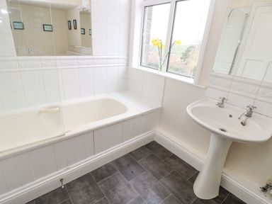 A bathroom with a bathtub a pedestal sink a window with flowers on the sill and a tiled floor at Heatherbrae in Middleton-In-Teesdale