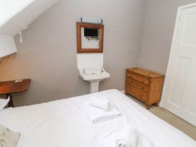 A bedroom with a bed folded towels a wooden chest of drawers a wall mounted mirror and sink at Heatherbrae in Middleton-In-Teesdale