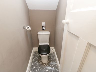 A small bathroom with a toilet that has a black seat and mosaic tile floor at Heatherbrae in Middleton-In-Teesdale