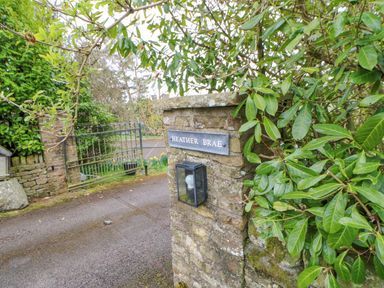 A stone pillar with a lamp and a sign reading Heather Brae next to a metal gate and greenery at Heatherbrae in Middleton-In-Teesdale