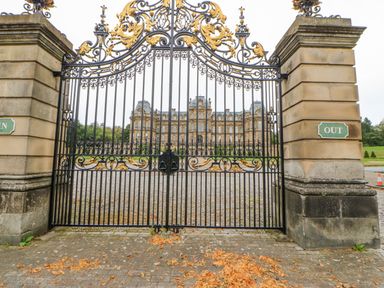 An ornate black and gold iron gate between stone pillars with a large mansion visible behind the gate at Heatherbrae in Middleton-In-Teesdale