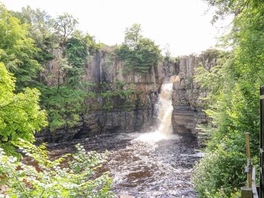 A waterfall flowing into a river surrounded by cliffs and green trees at Heatherbrae in Middleton-In-Teesdale