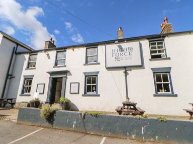 Exterior view of a white building with black window frames and a sign reading High Force Hotel and Waterfall with outdoor benches
