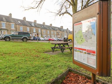 A street with parked cars stone houses a picnic table a litter bin and an information board at Heatherbrae in Middleton-In-Teesdale