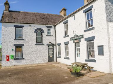 White stone building with multiple windows and a sign reading Langdon Beck Hotel with a picnic bench and planter outside at Heatherbrae in Middleton-In-Teesdale