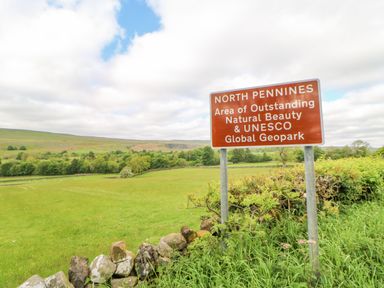 A countryside landscape with a road sign indicating North Pennines Area of Outstanding Natural Beauty and UNESCO Global Geopark at Heatherbrae in Middleton-In-Teesdale