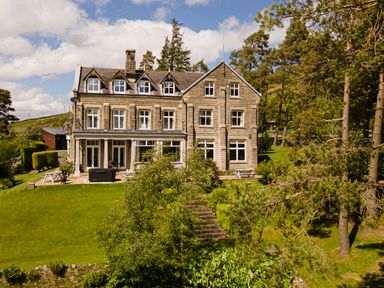 A large stone house with multiple windows surrounded by trees and a grassy lawn at Heatherbrae in Middleton-In-Teesdale