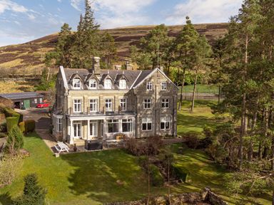 A large stone house with multiple windows and a patio in a grassy area with trees at Heatherbrae in Middleton In Teesdale