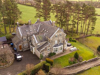 A stone house surrounded by trees and green fields with a driveway and parked car at Heatherbrae in Middleton-In-Teesdale