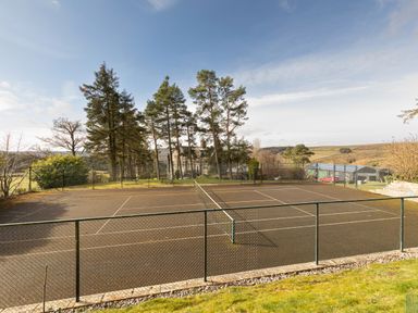 An outdoor tennis court with a fence around it surrounded by trees and countryside at Heatherbrae in Middleton-In-Teesdale