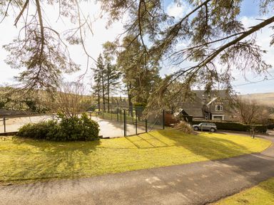 Outdoor tennis court with fence surrounded by grass and trees near a house with a driveway at Heatherbrae in Middleton-In-Teesdale