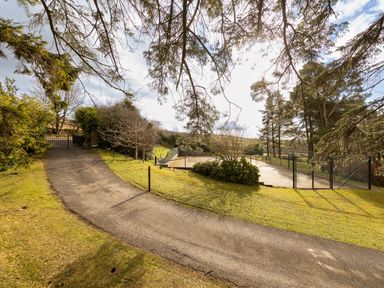 A paved driveway leading to a gate with trees and a fenced tennis court at Heatherbrae in Middleton-In-Teesdale