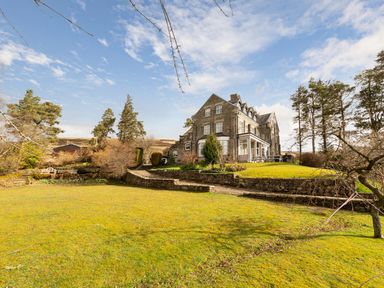 A large stone house with multiple windows and a garden with trees and grass at Heatherbrae in Middleton-In-Teesdale