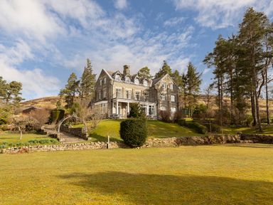 A large stone house with multiple windows surrounded by trees and a grassy lawn at Heatherbrae in Middleton-In-Teesdale