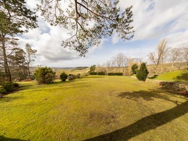 An open grassy garden area with scattered trees and shrubs and hills in the background at Heatherbrae in Middleton-In-Teesdale