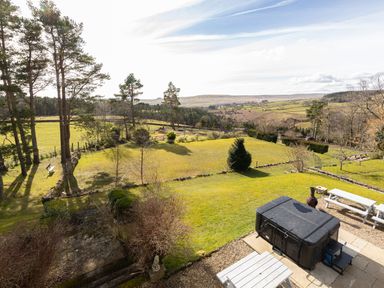 A garden area with trees picnic tables hot tub and distant hills at Heatherbrae in Middleton-In-Teesdale