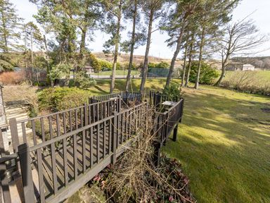 A wooden deck with railings overlooking a grassy garden with trees at Heatherbrae in Middleton-In-Teesdale