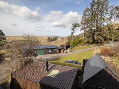 A rural outdoor scene with multiple wooden buildings including one with solar panels and a car parked on a driveway at Heatherbrae in Middleton-In-Teesdale