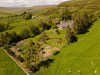 A large house with surrounding gardens trees and sheep grazing in green fields at Heatherbrae in Middleton-In-Teesdale