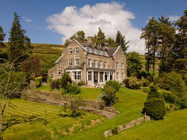 A large stone house with a garden and trees on a hillside at Heatherbrae in Middleton-In-Teesdale