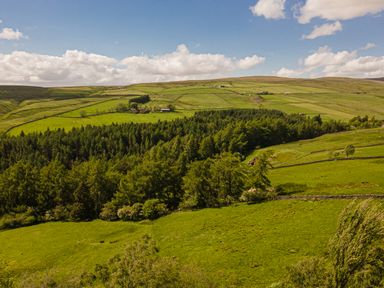 Green hills with patches of forest and farmland under a partly cloudy sky at Heatherbrae in Middleton-In-Teesdale