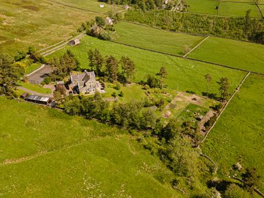 An aerial view of a large house surrounded by trees gardens fenced fields and sheep grazing at Heatherbrae in Middleton-In-Teesdale